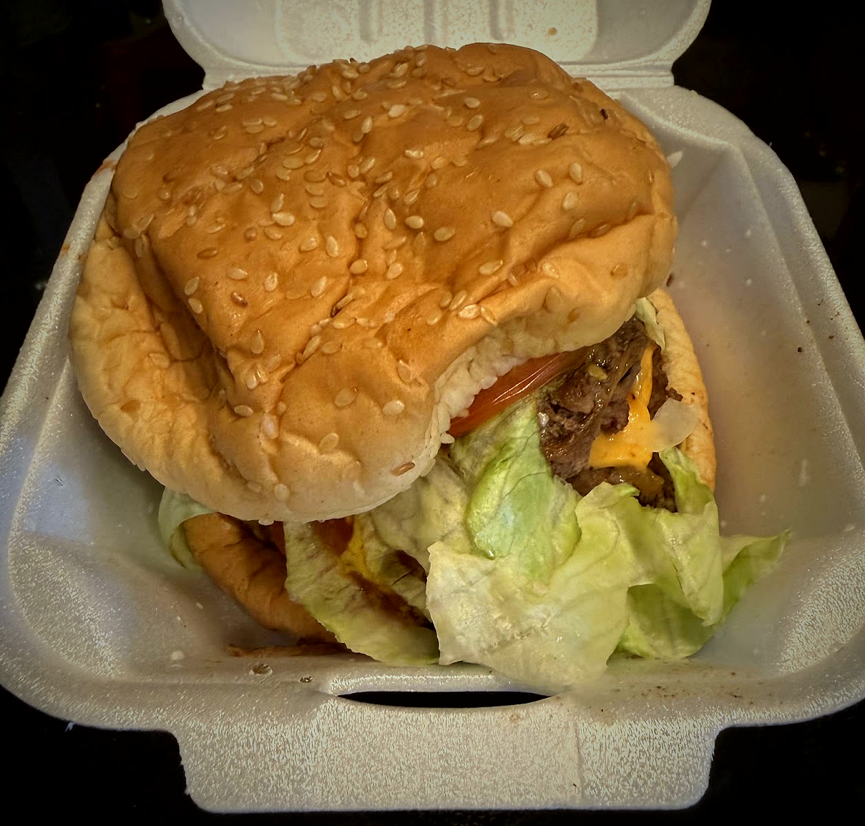 A large double cheeseburger with lettuce and tomato in a takeout container.