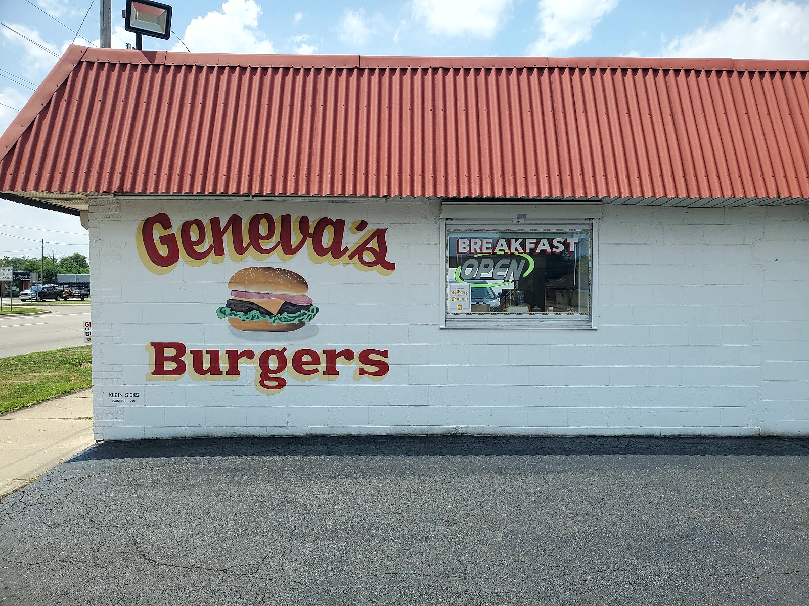 The side of Geneva's Burgers, white block wall with the name hand painted in red beside a painted burger.