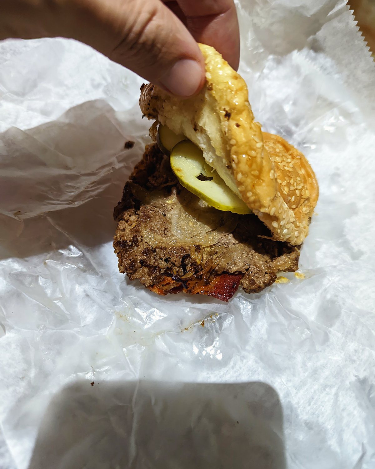 A hand lifting the top bun off a Geneva's burger to show the patty and pickles.