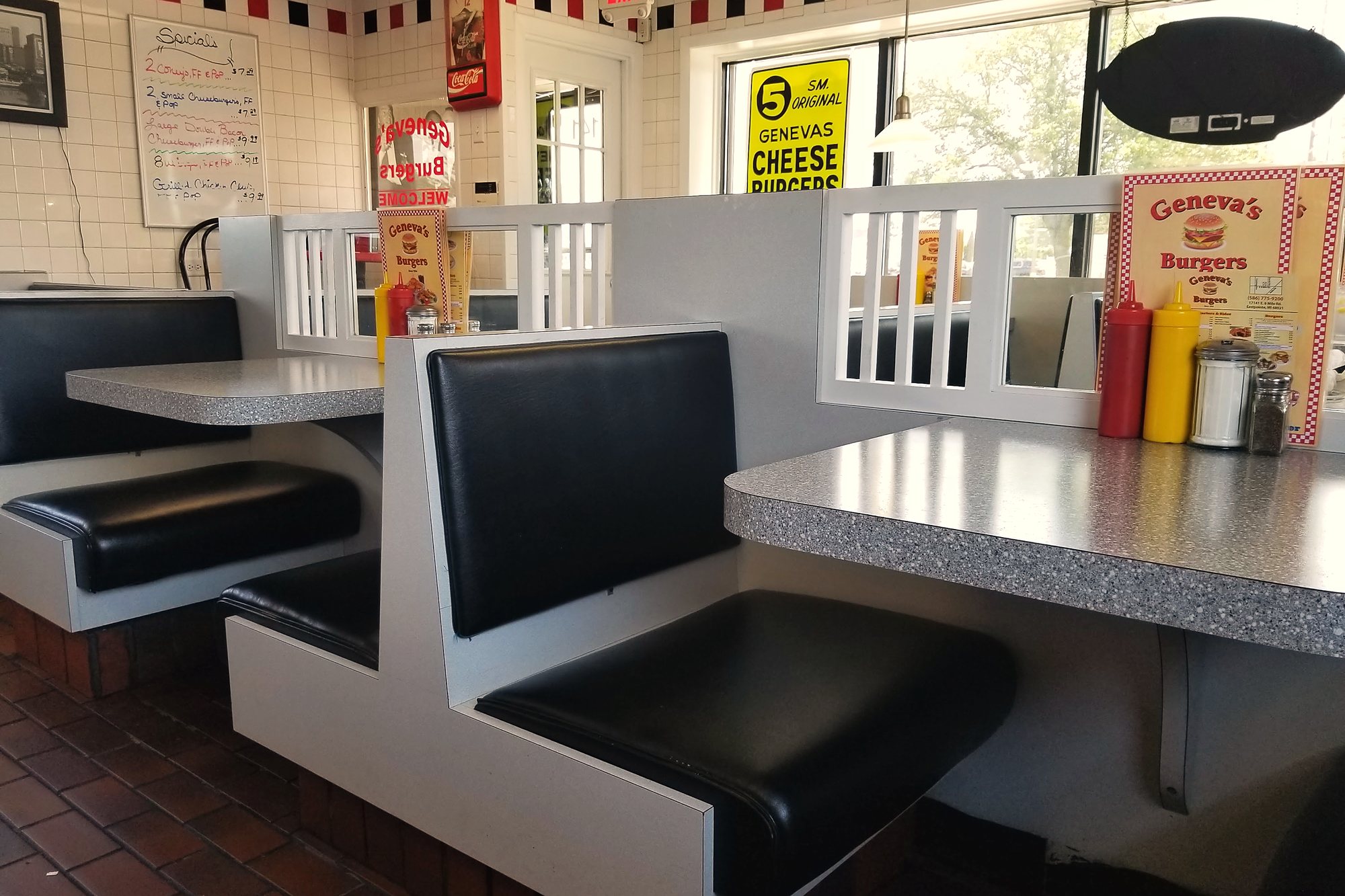 Inside Geneva's, black vinyl booths by the windows with checkered trim along the wall.